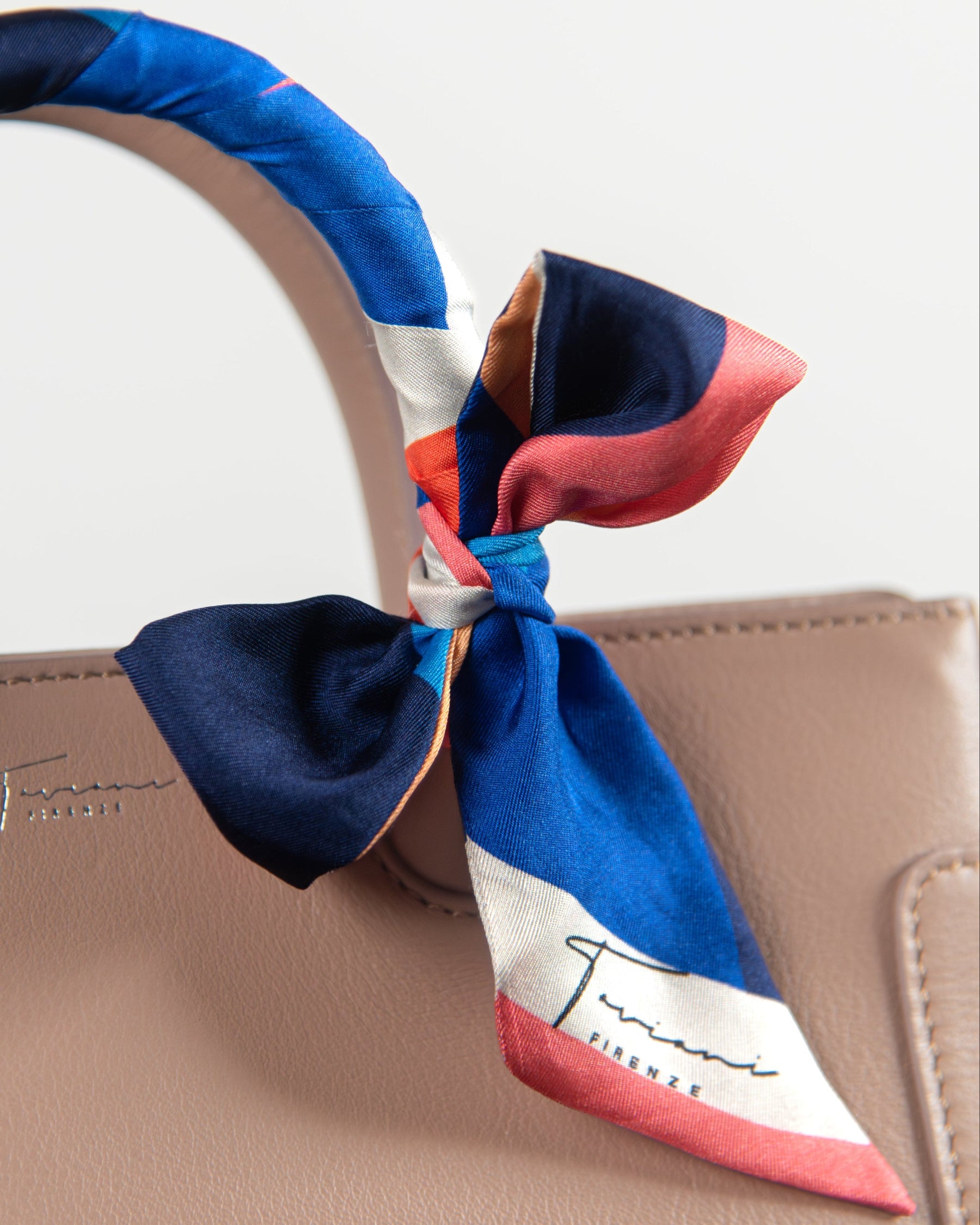 Colorful scarf tied around a handbag handle with a visible brand logo.