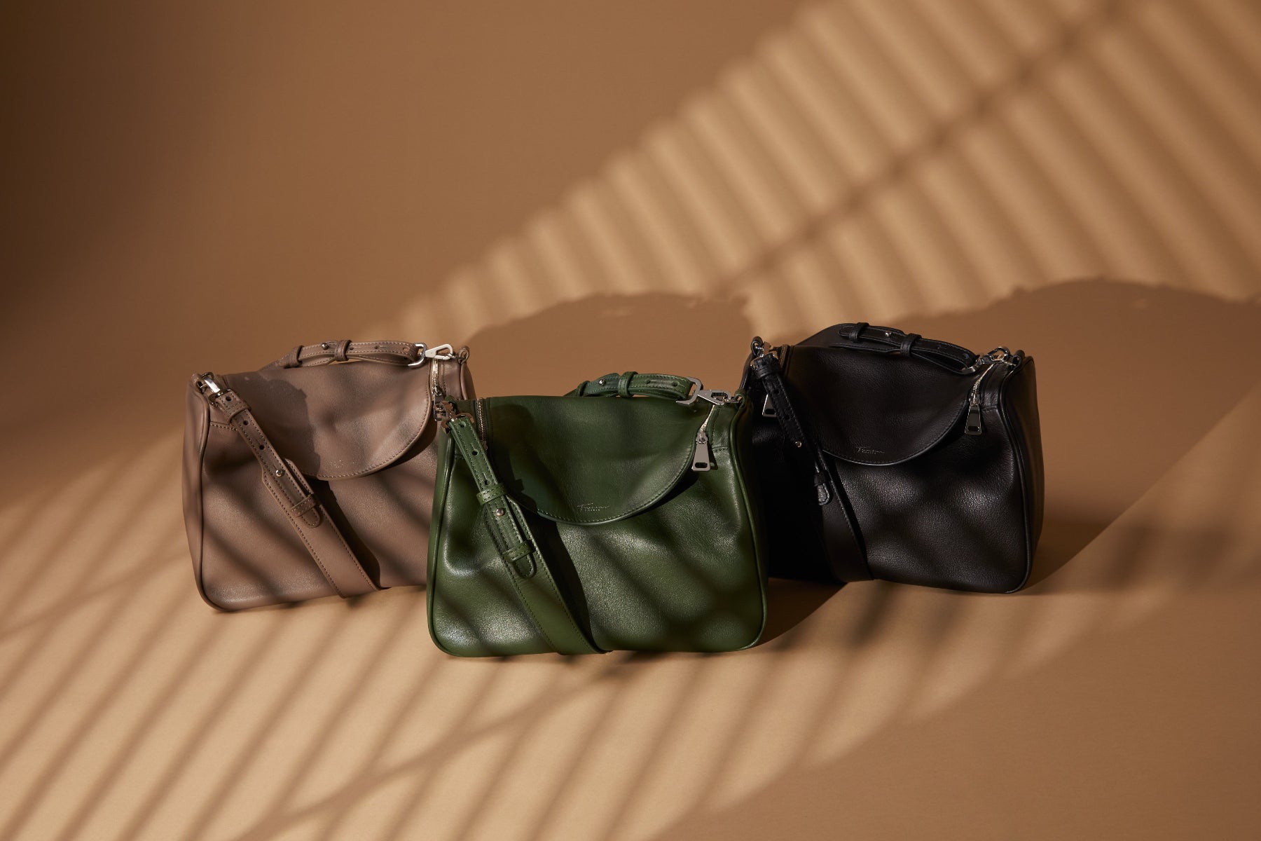 Three leather handbags in beige, green, and black on a brown background