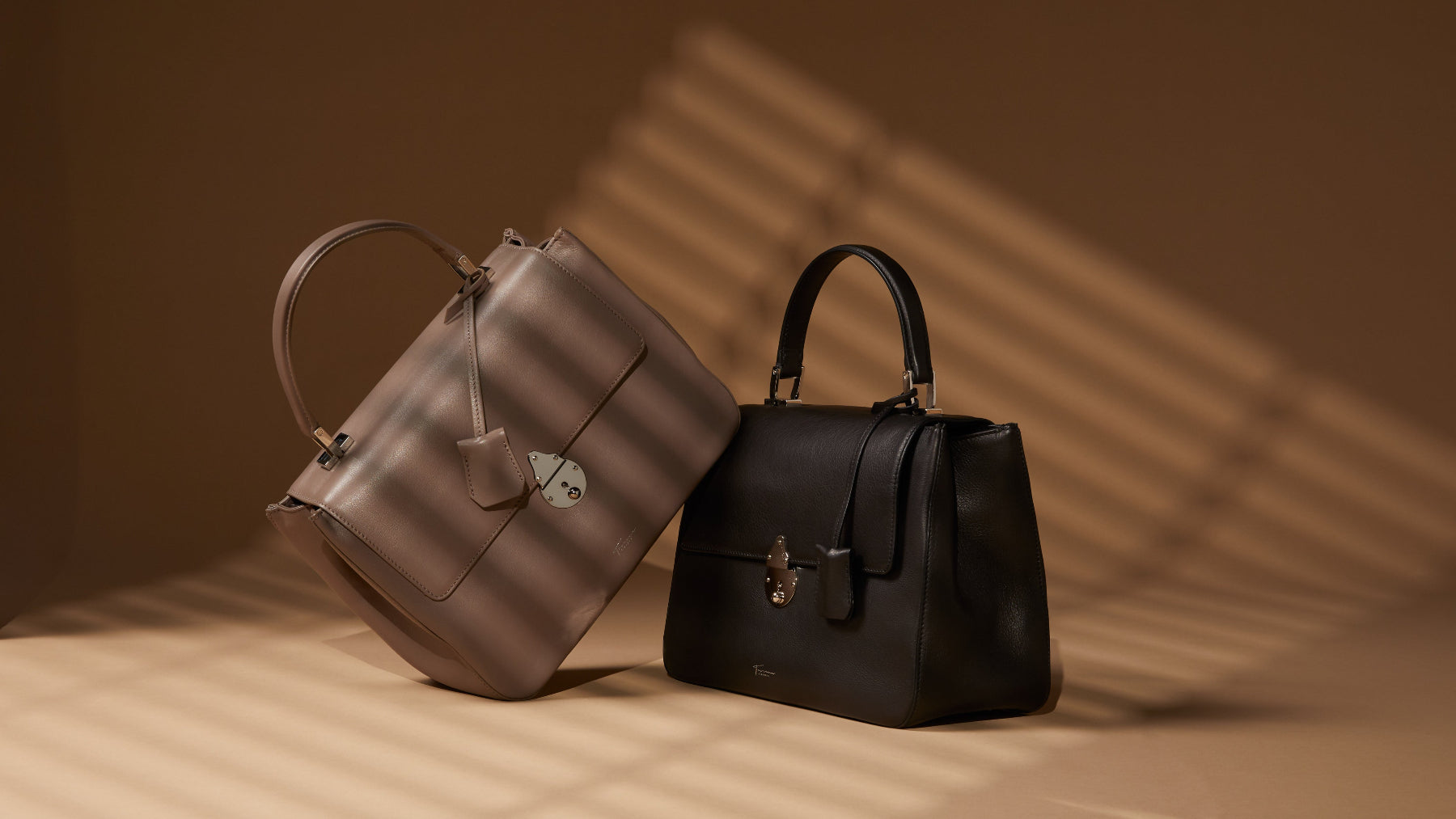 Two handbags, one silver and one black, on a textured surface with a warm brown background.