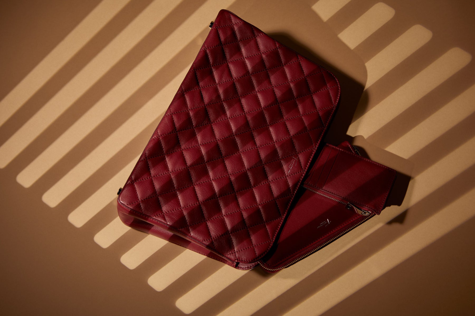 Red quilted leather bag on a brown background with shadow patterns