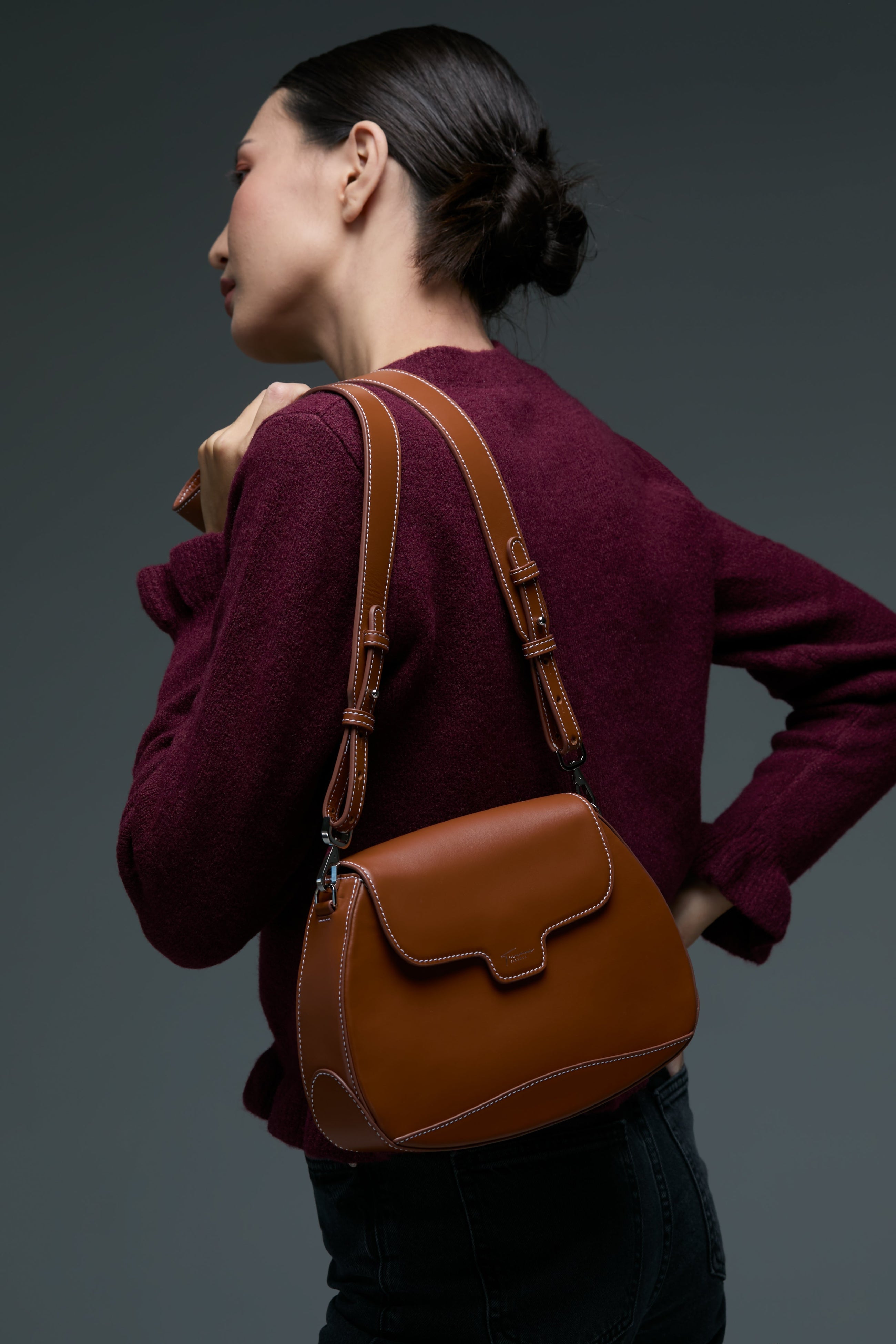 Woman wearing a brown leather shoulder bag against a dark background